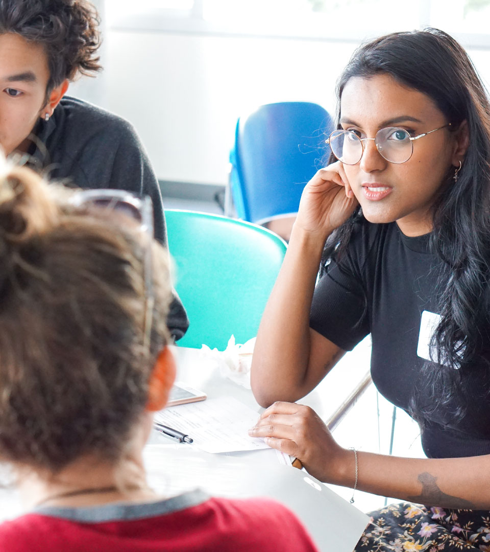 Three people site and chat around a table